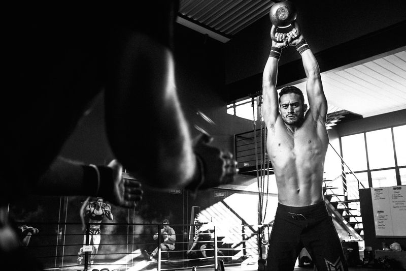 César Ribeiro levantando um kettlebell acima da cabeça, olhando para a câmera.